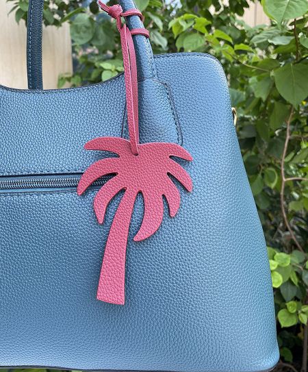 A pink coconut tree leather keychain attached to a stylish blue handbag.
