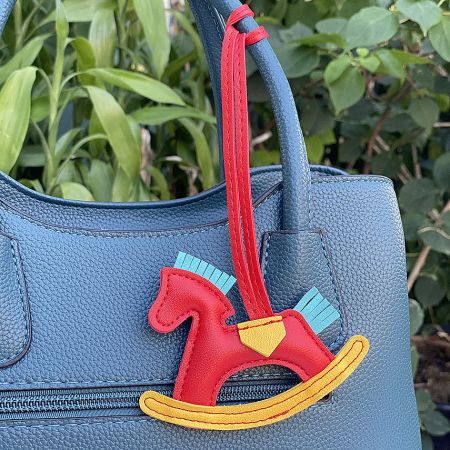A vibrant red rocking horse keychain adding a playful touch to a blue leather bag.