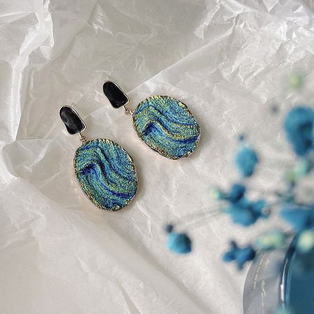 A pair of earrings with a unique blue and green marbled design, set in gold with a black stone accent.