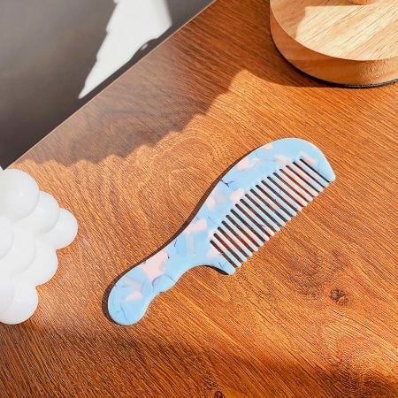 A beautiful blue and pink marbled wide-tooth comb on a neutral background.