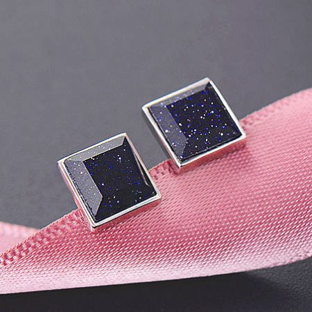 A pair of purple sandstone earrings displayed on a pink ribbon.