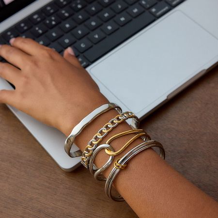 Lifestyle image showing a stack of two-tone gold and silver bangles worn on a wrist.