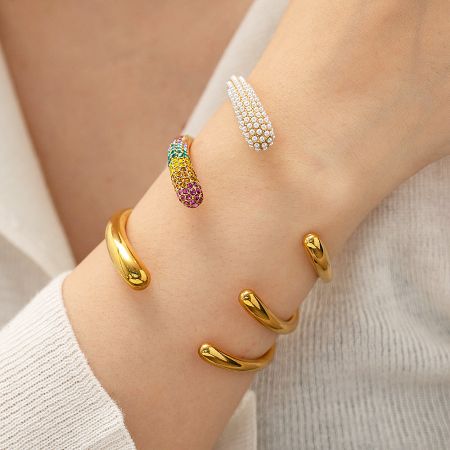 A model's wrist adorned with multiple gold bangles from the colorful CZ and pearl set.