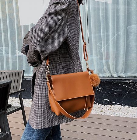 Large Capacity Cross Body Bag Wholesale - A stylish woman wearing the large capacity brown PU leather crossbody bag with a decorative pom-pom keychain, showcasing its design and size.