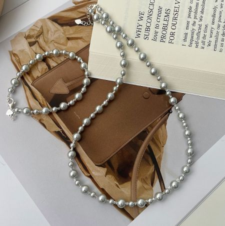 925 Sterling Silver Grey Pearl Necklace Bracelet - A sophisticated 925 sterling silver grey pearl necklace and bracelet set, elegantly displayed next to a classic brown leather purse.