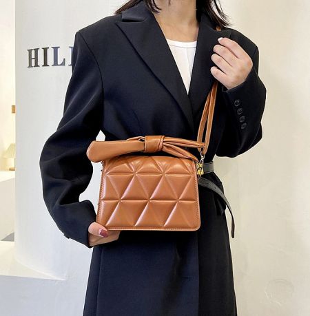 Close-up of the brown ribbon quilted PU leather handbag held by a model.