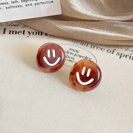 Un par de pendientes de cara sonriente marrones exhibidos sobre un fondo de tela.