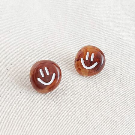 Toma detallada de los pendientes de cara sonriente marrones y brillantes, mostrando el acabado del material.