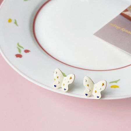 Another angle of the butterfly earrings on a decorative plate, showcasing the product's finish.