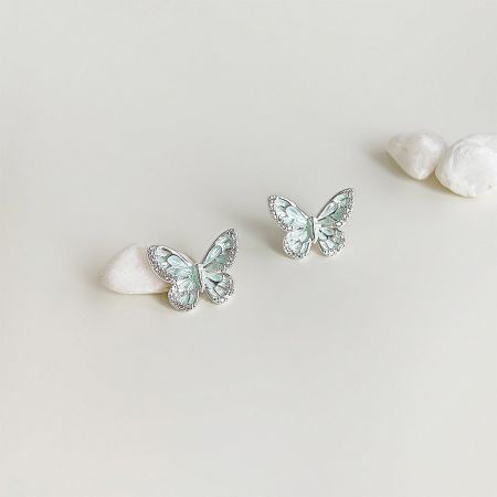 A pair of mint green butterfly earrings with silver details on a neutral background.