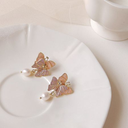 Close-up view of the butterfly earrings, highlighting the pink and purple enamel details and gold outlines.