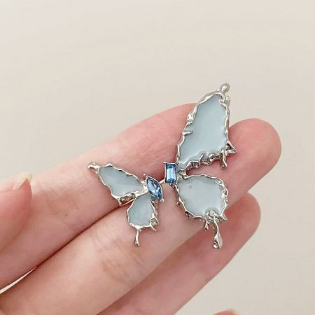 The butterfly earring design shown as a pendant, highlighting the central blue gemstone.