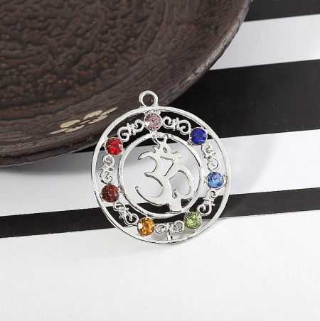 A circular silver chakra pendant featuring the Om symbol surrounded by seven colored gemstones.