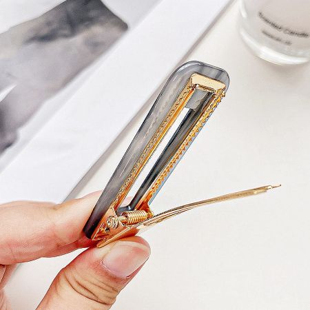 A hand holding a clear acrylic hair clip with elegant gold metal details.