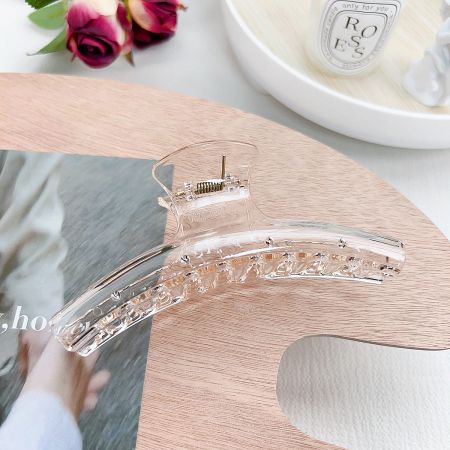 Detailed view of the transparent hair clip highlighting the strong gold spring mechanism.