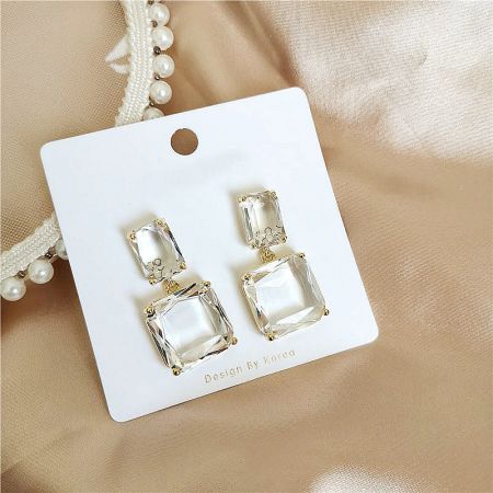 Close-up of the clear rectangular crystal earrings on a 'Design By Korea' display card.