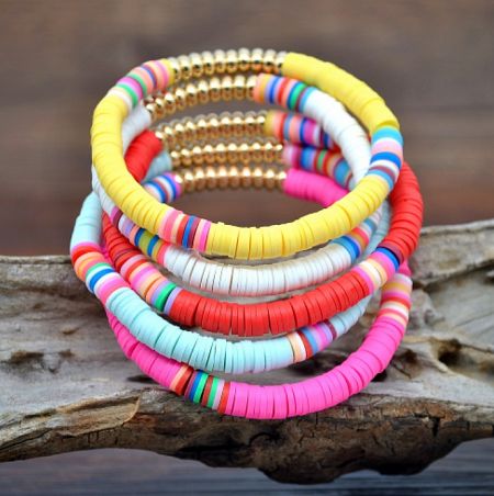 A collection of colorful beaded bracelets, including the Bohemia polymer clay style, displayed on a piece of driftwood.
