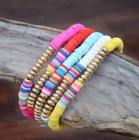 Detailed view of the colorful polymer clay and gold bead bracelets arranged artistically on natural driftwood.