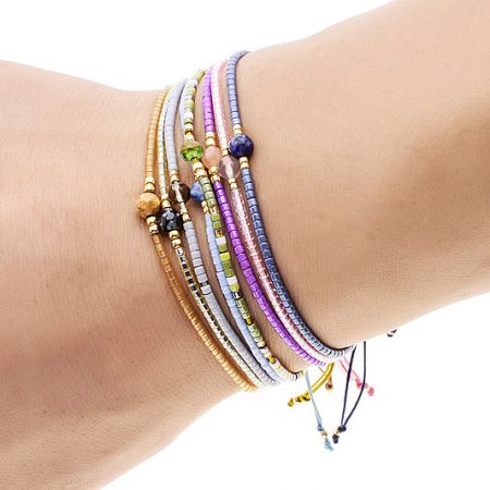 A vibrant set of multi-color bohemian rice bead and natural stone bracelets worn on a wrist.