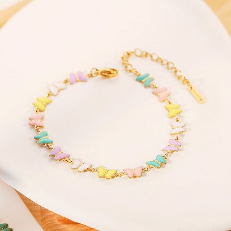 A close-up view of the gold chain bracelet adorned with colorful pastel butterfly-shaped beads.