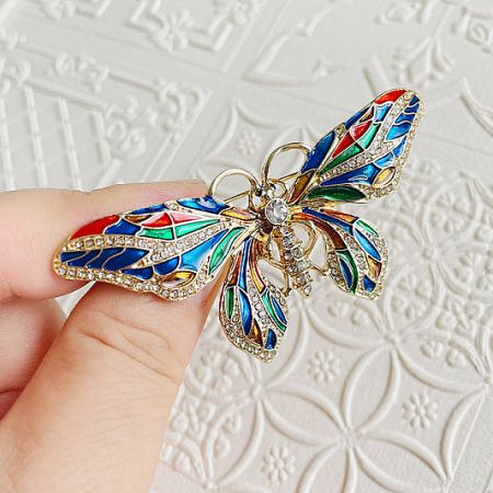 Colorful enamel butterfly brooch with stained-glass style wings and gemstone accents.