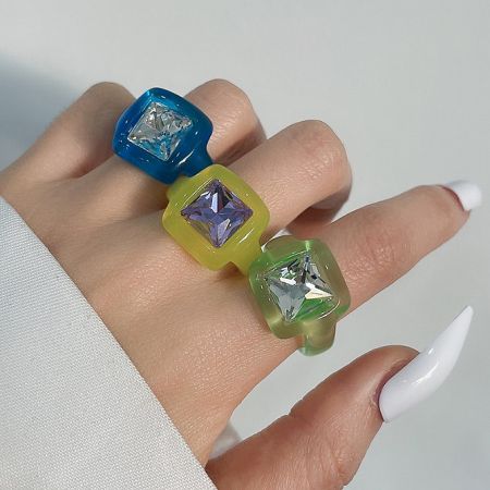 Three colorful acrylic rings with rhinestones worn on a hand to display their look and fit.