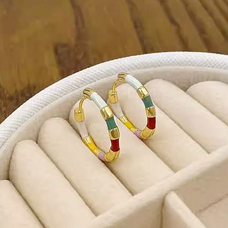 A pair of colorful enamel hoop earrings with gold accents elegantly displayed in a white jewelry box.