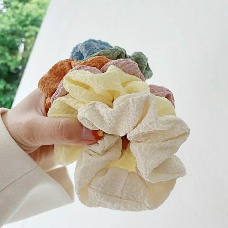 A close-up shot of various colorful scrunchies made from soft, textured fabric.