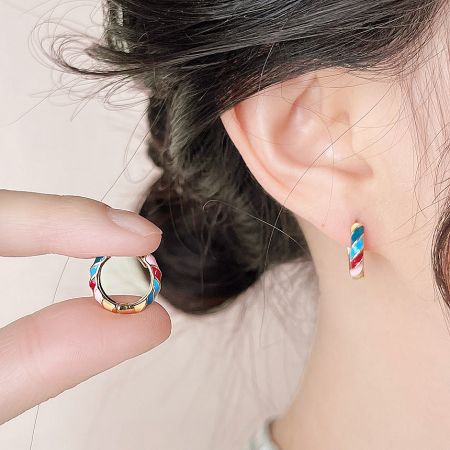 A pair of gold huggie hoops with red, white, and blue enamel twist design.