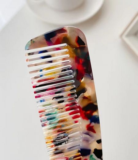 Close-up of a colorful wide-tooth acetate comb with a marbled pattern.