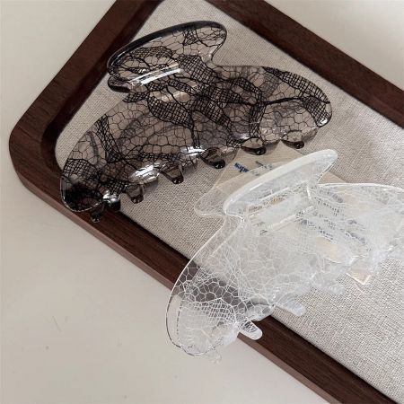 A pair of stylish hair claw clips in black and clear with an elegant lace pattern.