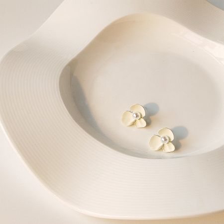 The cream-colored flower earrings with pearls displayed on a white ceramic dish.