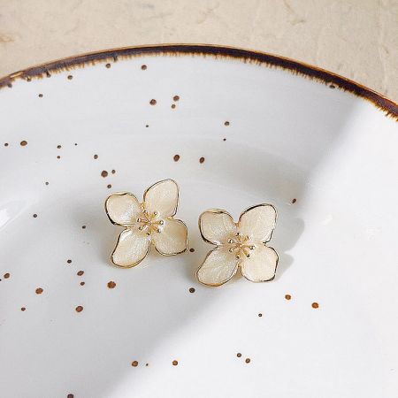 A pair of cream and gold flower earrings displayed on a decorative plate.