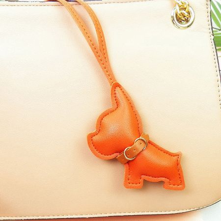 A cream-colored leather bag adorned with a vibrant orange French Bulldog charm.