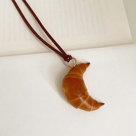 Detailed view of the golden-brown croissant-shaped pendant necklace.