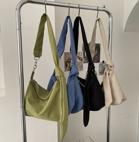 Four crossbody sling bags in various colors including army green, light blue, and black, displayed on a rack to showcase the collection.