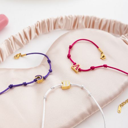 Wholesale enamel letter friendship bracelets with A, B, C initials displayed in a soft satin pouch, perfect for personalized gifts.