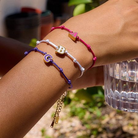 Model wearing a stack of three adjustable friendship bracelets with custom A, B, and C enamel letter charms.