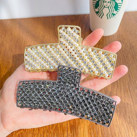 A hand holding two hair clips, one silver and one gold with pearls, showing the different style options.