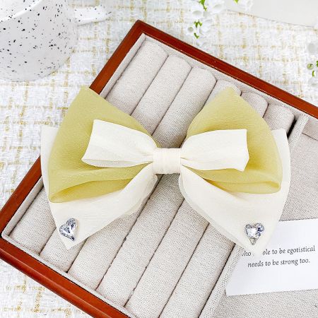 Close-up of a ribbon bow hair clip featuring a delicate heart-shaped gem embellishment.