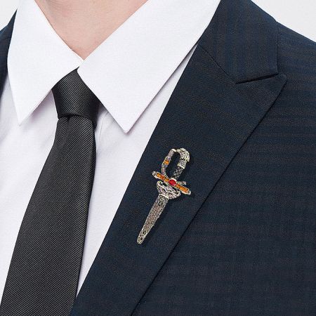 A detailed view of the decorative sword brooch pinned on a textured suit jacket, highlighting its craftsmanship.