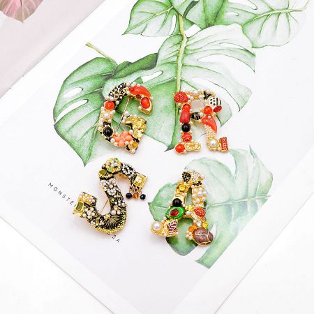 An artistic arrangement of Baroque letter brooches on monstera leaves, showcasing their versatile and decorative appeal.