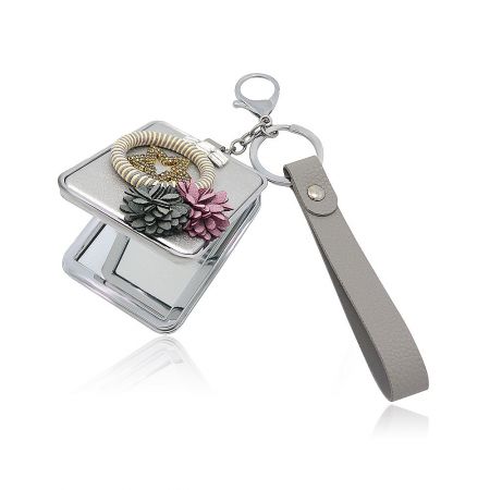 The compact mirror shown with various decorative elements including a beaded bracelet and pinecone charms, highlighting its versatility as a fashion accessory.