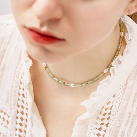Close-up of a delicate necklace featuring greenish-gray beads, white pearls, and subtle gold accents.