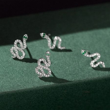 Close-up of diamond-encrusted snake earrings with striking green gemstone eyes.