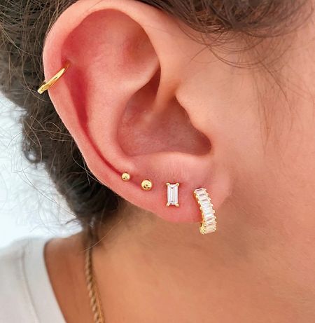 Close-up view of a gold huggie hoop earring with cubic zirconia worn on an ear.