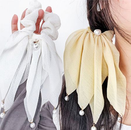 A person holding and wearing a fabric hair accessory with pearl embellishments.