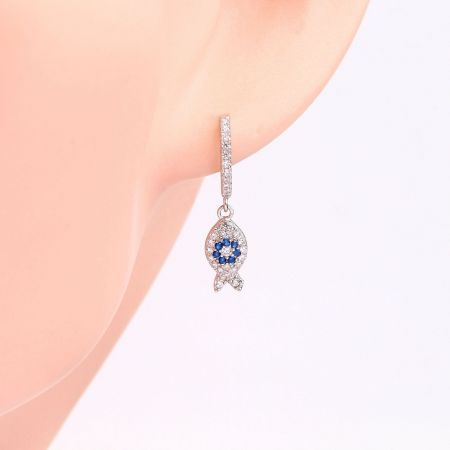 Close-up of a single fish-shaped huggie earring with sparkling blue and clear gemstones.