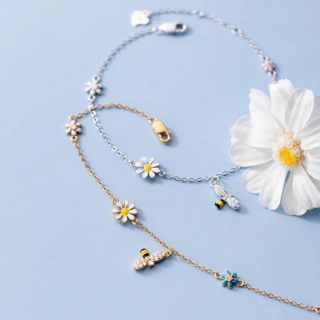 A pair of 925 sterling silver bracelets, one silver and one gold-plated, with daisy and bee charms.