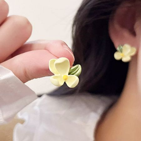 A hand holding one of the gardenia flower earrings to demonstrate its scale.
